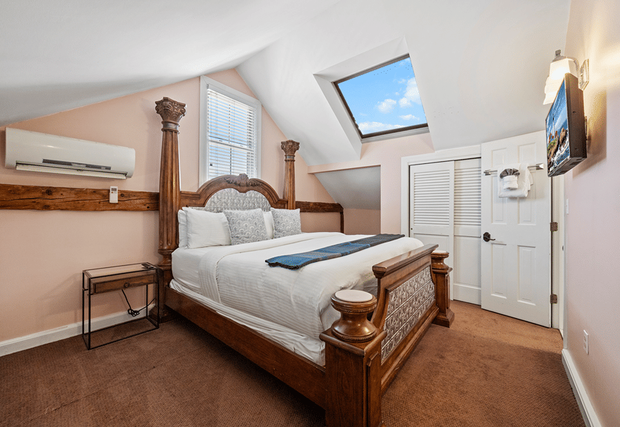 A wide view of a guest room with a large bed, skylight, and flat-screen TV.
