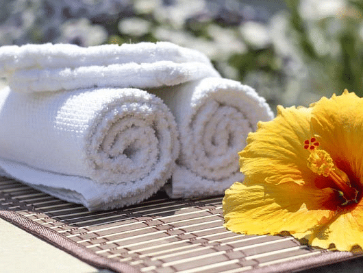 A yellow hibiscus flower on top of a table placed alongside freshly folded white towels.