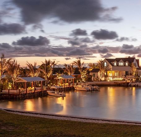 Waterfront buildings glow under dramatic evening skies, with lights reflecting off the calm water in a twilight setting | Abaco Inn