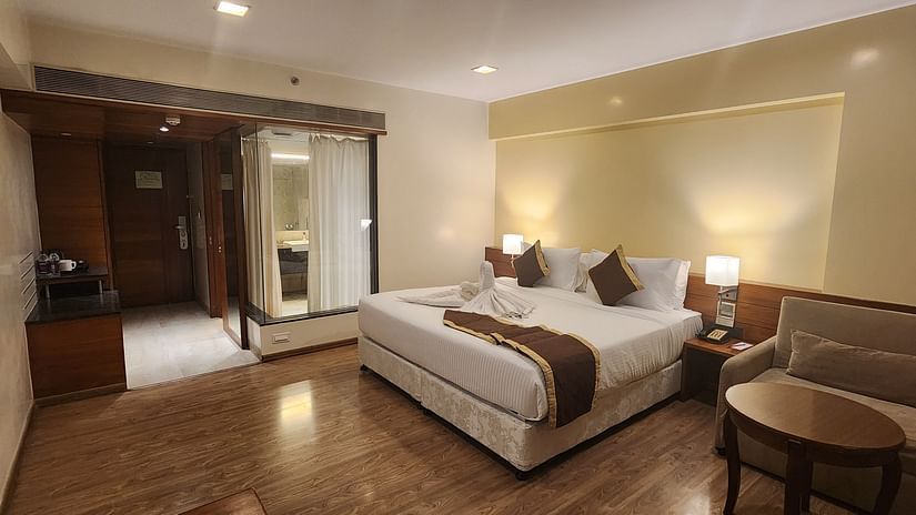 A well decorated bedroom with a large bed, a sofa, a coffee table, and a transparent glass bathroom with curtains.