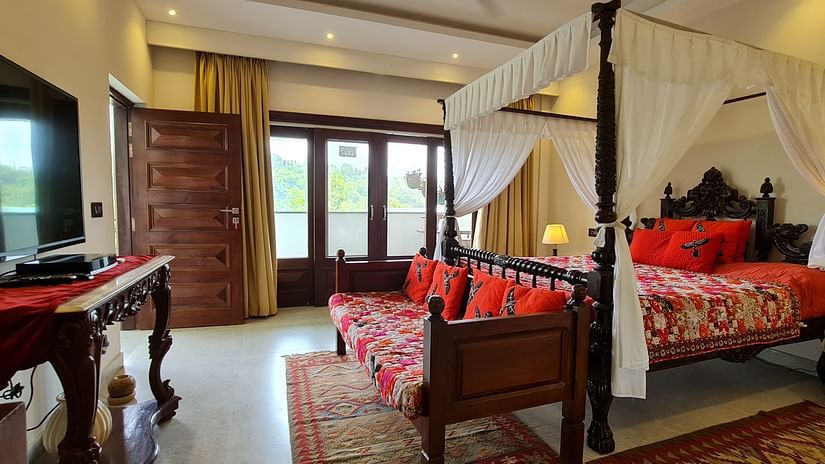 an opulent bedroom with a four-poster bed, vibrant red accents, and a large flat-screen TV at Shaheen Bagh Resort and Spa