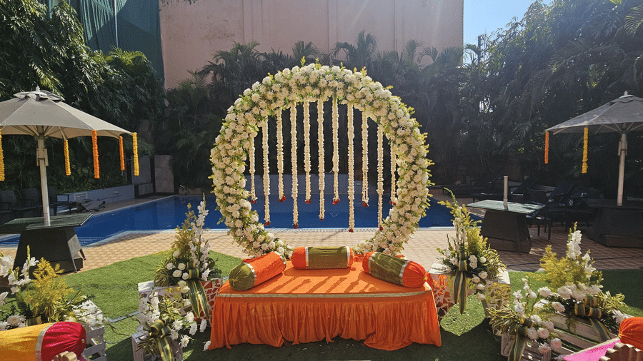 An outdoor event setup by a pool featuring a circular floral backdrop and an orange seating platform | HHI Varanasi