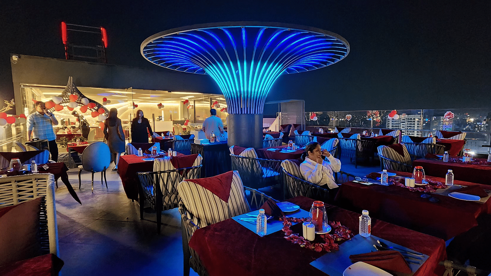A vibrant restaurant interior with modern blue lighting and red chairs, featuring a central decorative light fixture shaped like a mushroom.