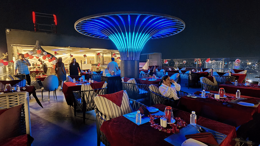 A vibrant restaurant interior with modern blue lighting and red chairs, featuring a central decorative light fixture shaped like a mushroom.