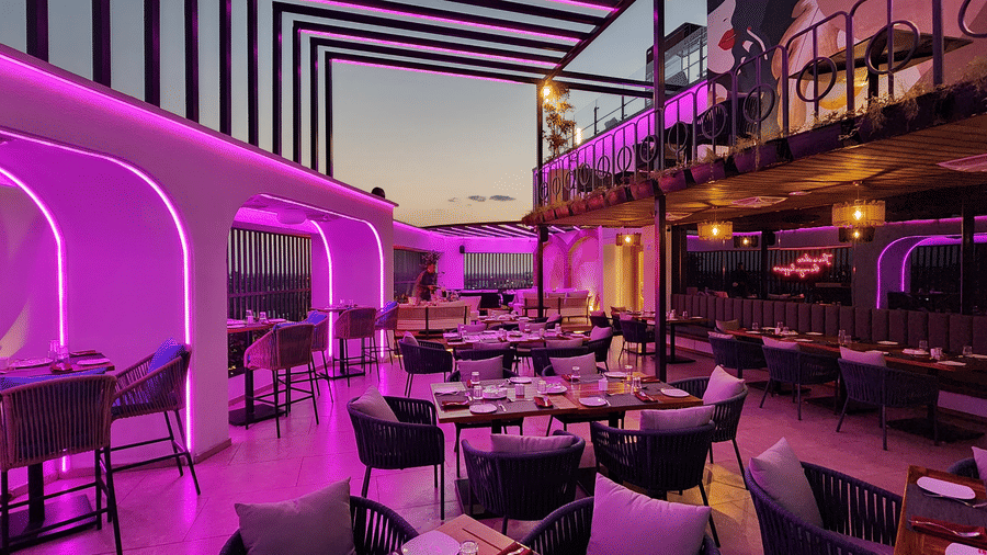 a rooftop dining area at Lords Inn Rajkot with variously arranged dining area on the floor, a balcony with seating area, and  a dimly lit ambience