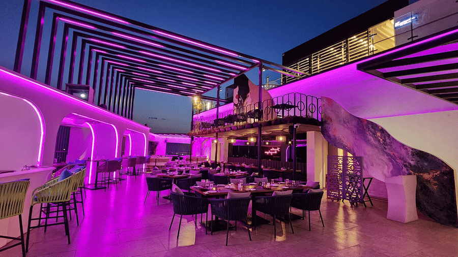 wide angle shot of the rooftop dining area at Lords Inn Rajkot with variously arranged dining area on the floor, a balcony with seating area, and  a dimly lit ambience