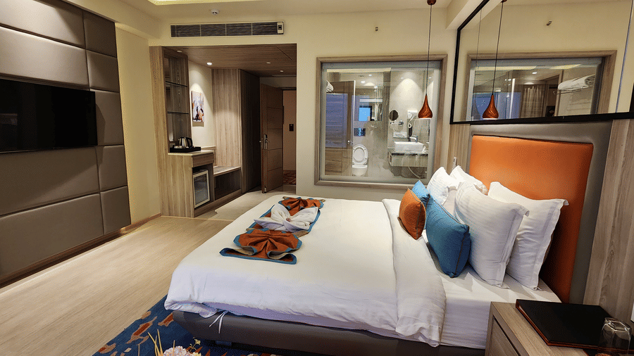 duplicate of a contemporary room with king size bed, wall-mounted TV, hanging lights, a full length mirror, and a glass panelled washroom at Lords Inn Rajkot