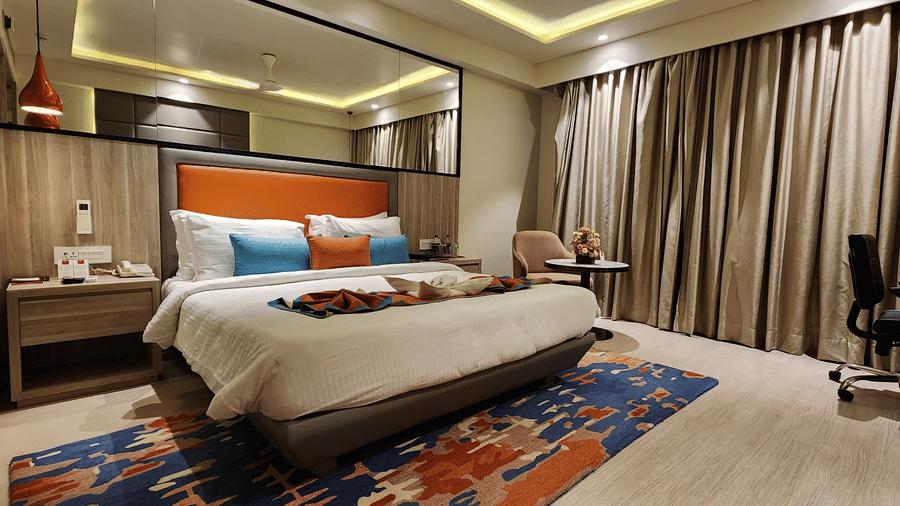 a spacious bedroom with a queen size bed, mirrored walls, warm lighting, and a workstation at Lords Inn Rajkot