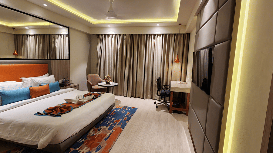 a close-up view of a bedroom with a king size bed, a workstation, wall-mounted TV, mirrored wardrobe, floor-to-ceiling curtains, and soft lighting at Lords Inn Rajkot