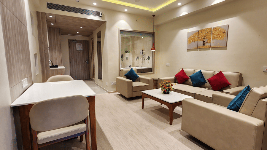 a lounge area of a semi-suite room at Lords Inn Rajot with ample of seating space, a coffee table, and a glass panelled washroom