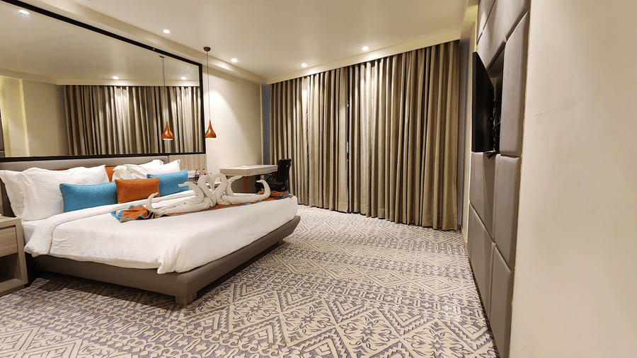 a luxurious with a king size bed, wall-mounted TV, mirrored wardrobe, floor-to-ceiling curtains, and soft lighting at Lords Inn Rajkot