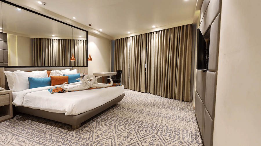 duplicate of a bedroom with a king size bed, wall-mounted TV, mirrored wardrobe, floor-to-ceiling curtains, and soft lighting at Lords Inn Rajkot