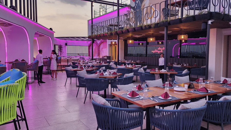 duplicate of a rooftop dining area at Lords Inn Rajkot with variously arranged dining area on the floor, a balcony with seating area, and a dimly lit ambience
