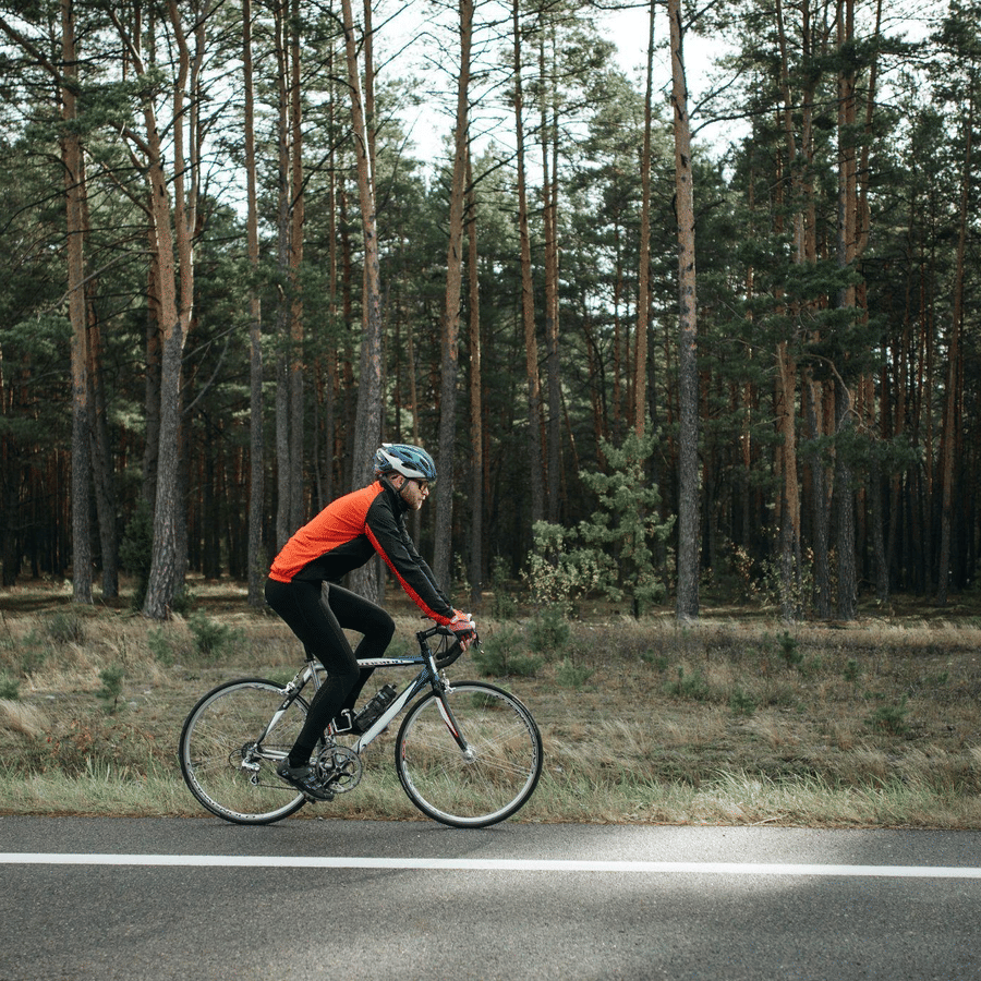 Cyclist riding along a forest road wearing a helmet and red jacket, enjoying an active outdoor adventure amidst tall pine trees