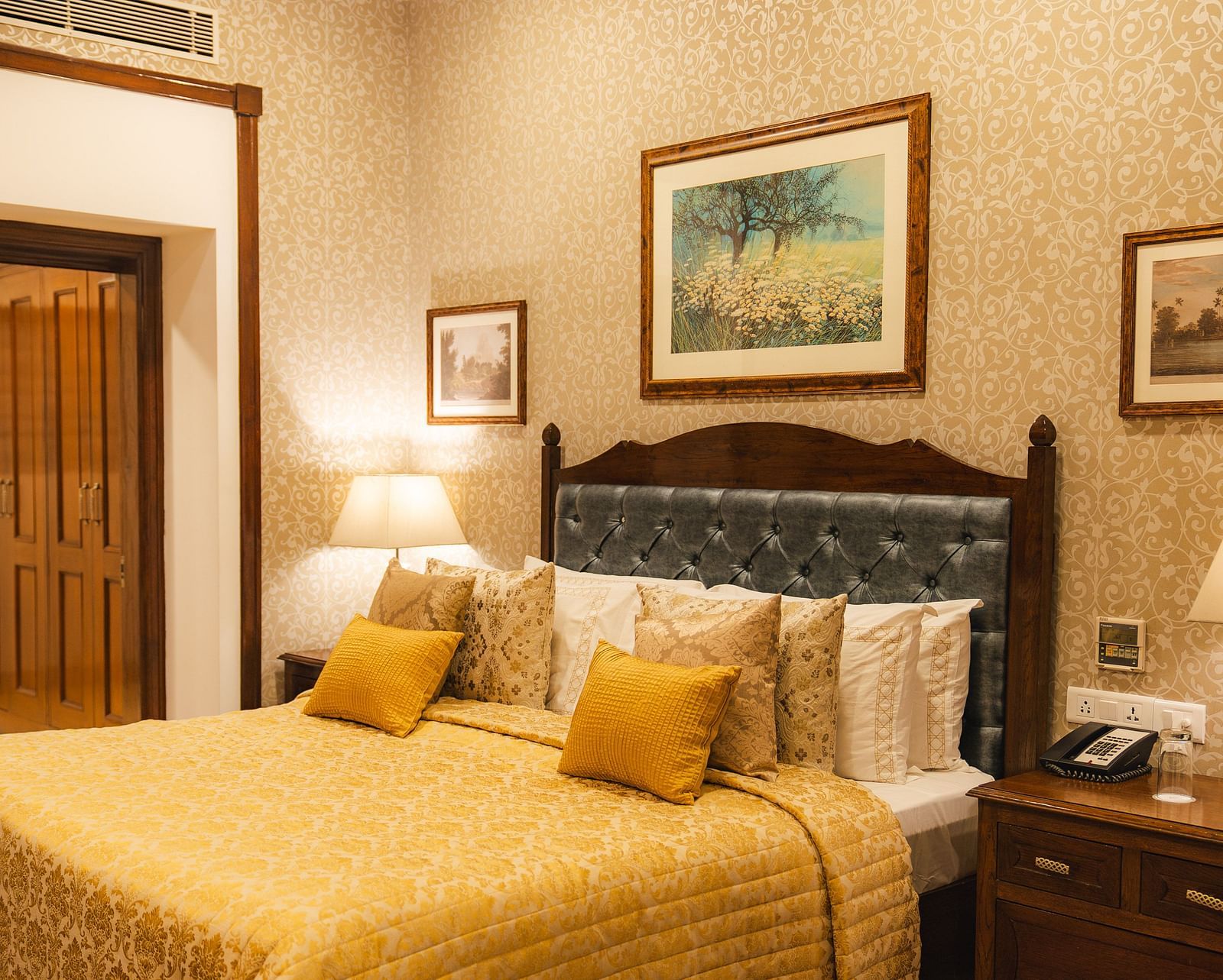 Cosy bedroom with patterned wallpaper, framed art, quilted bed, and warm lighting.