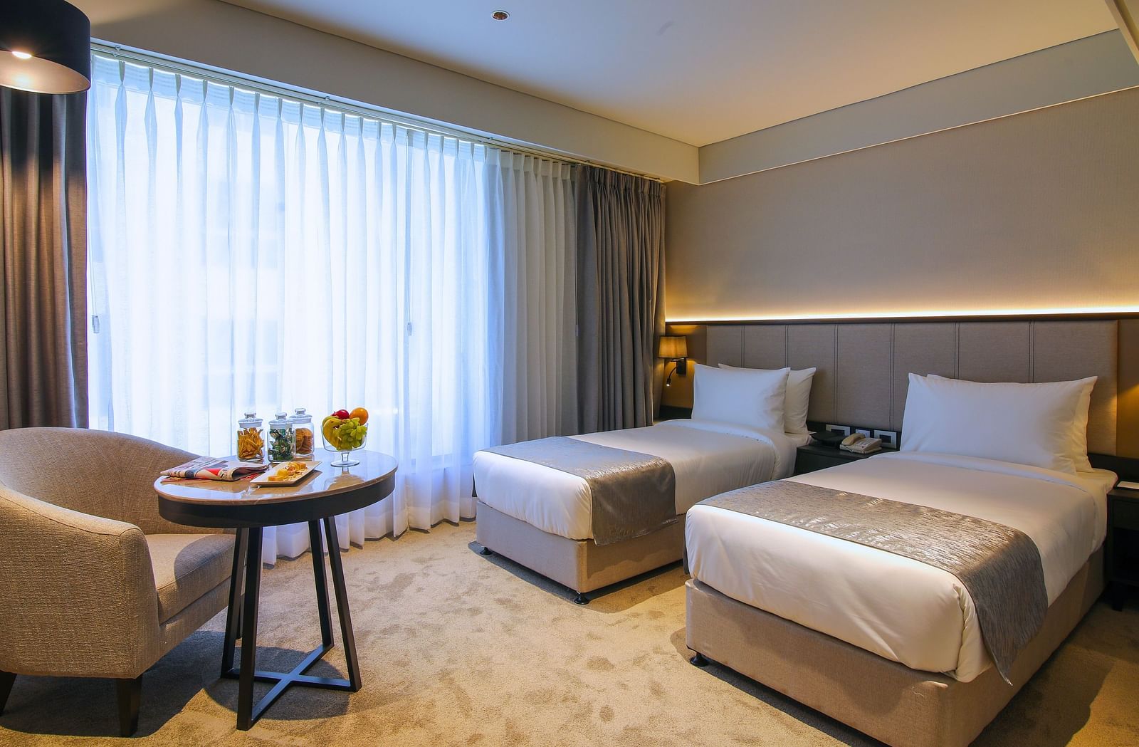 Twin beds with a chair and table in front of it inside one of the rooms - Essentia Premiere, Pune