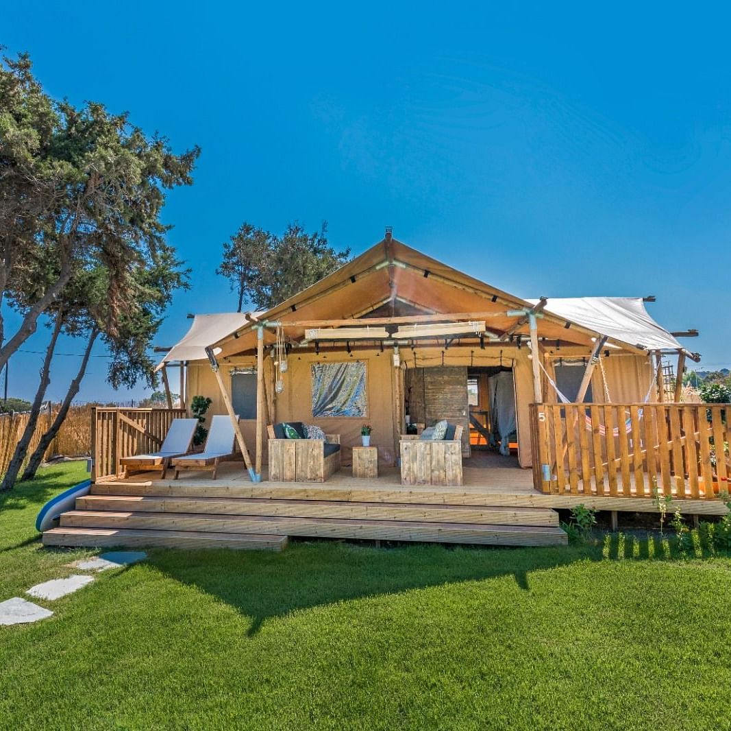 A luxurious tented villa with a wooden deck, outdoor seating, and a serene green lawn under a clear blue sky - WoCAL Retreat Ke Ga,