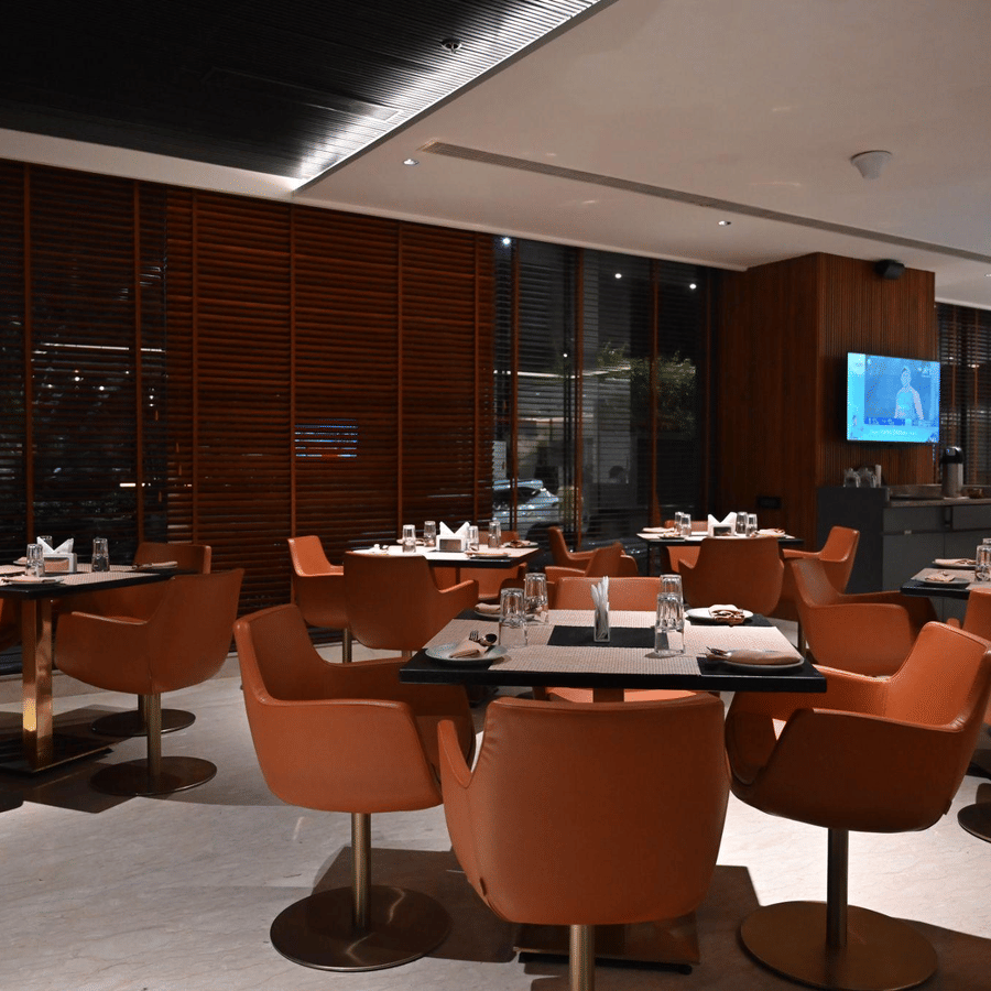 A contemporary dining area with round tables and orange chairs set against a warm, wooden backdrop.
