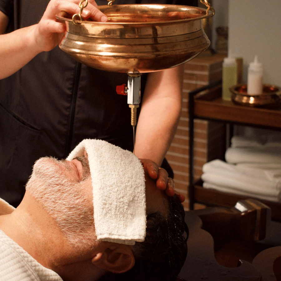 A person receives a traditional Ayurvedic oil therapy with a cloth over their eyes in a serene spa treatment room