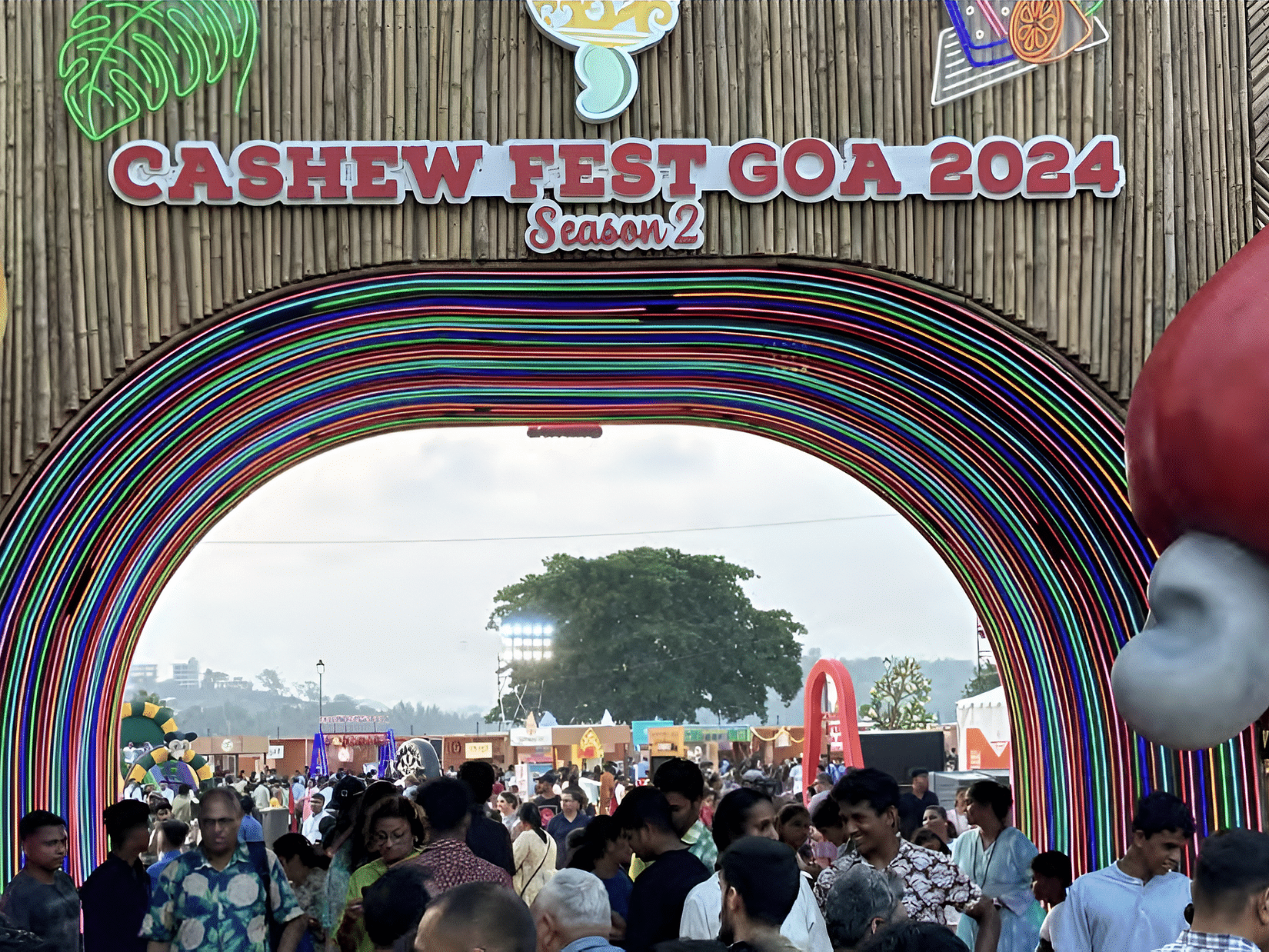 A crowded entrance decorated for the Cashew Fest Goa 2024 with balloons and banners. 