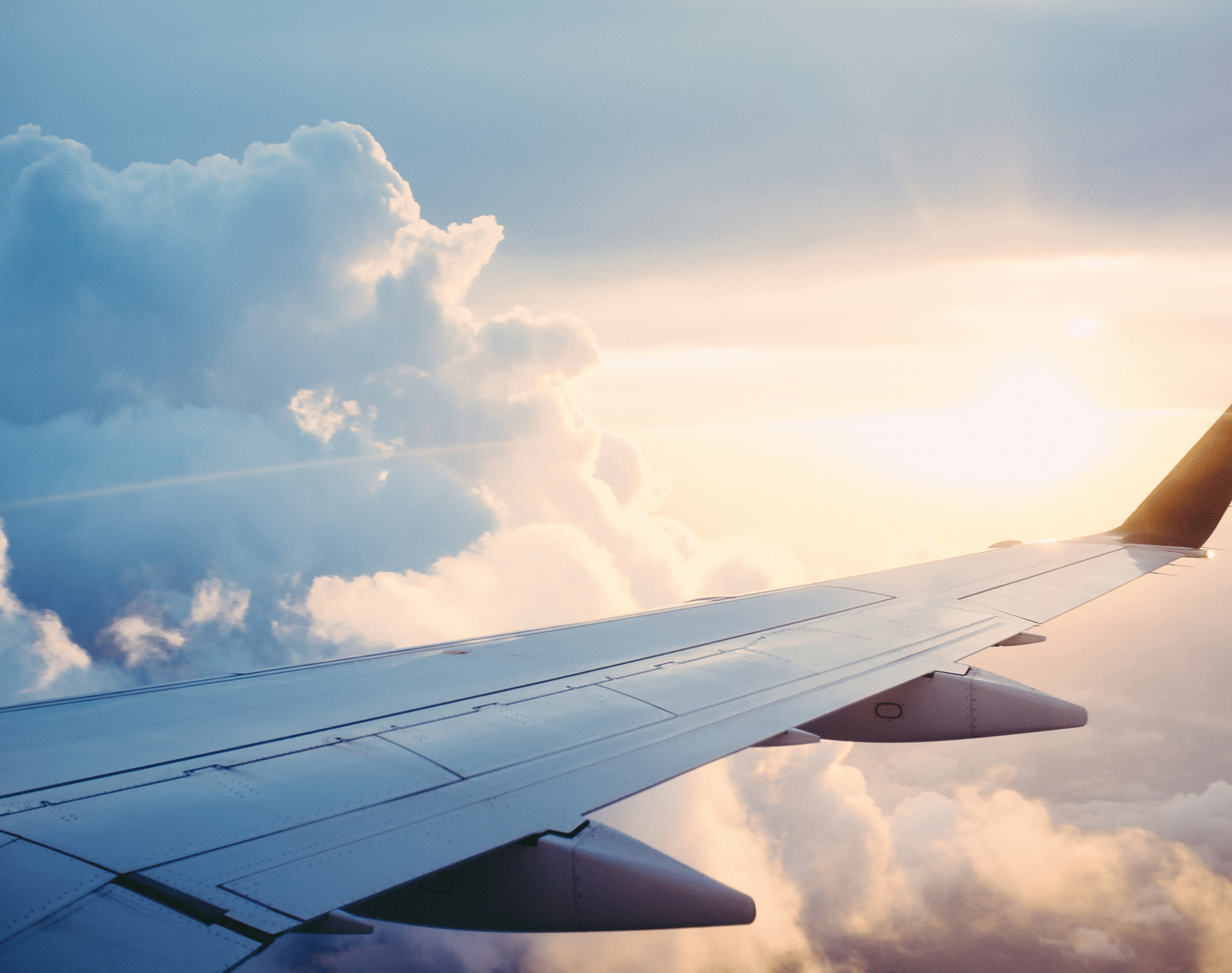 Sunlight glimmers on an airplane wing, flying high above the clouds.