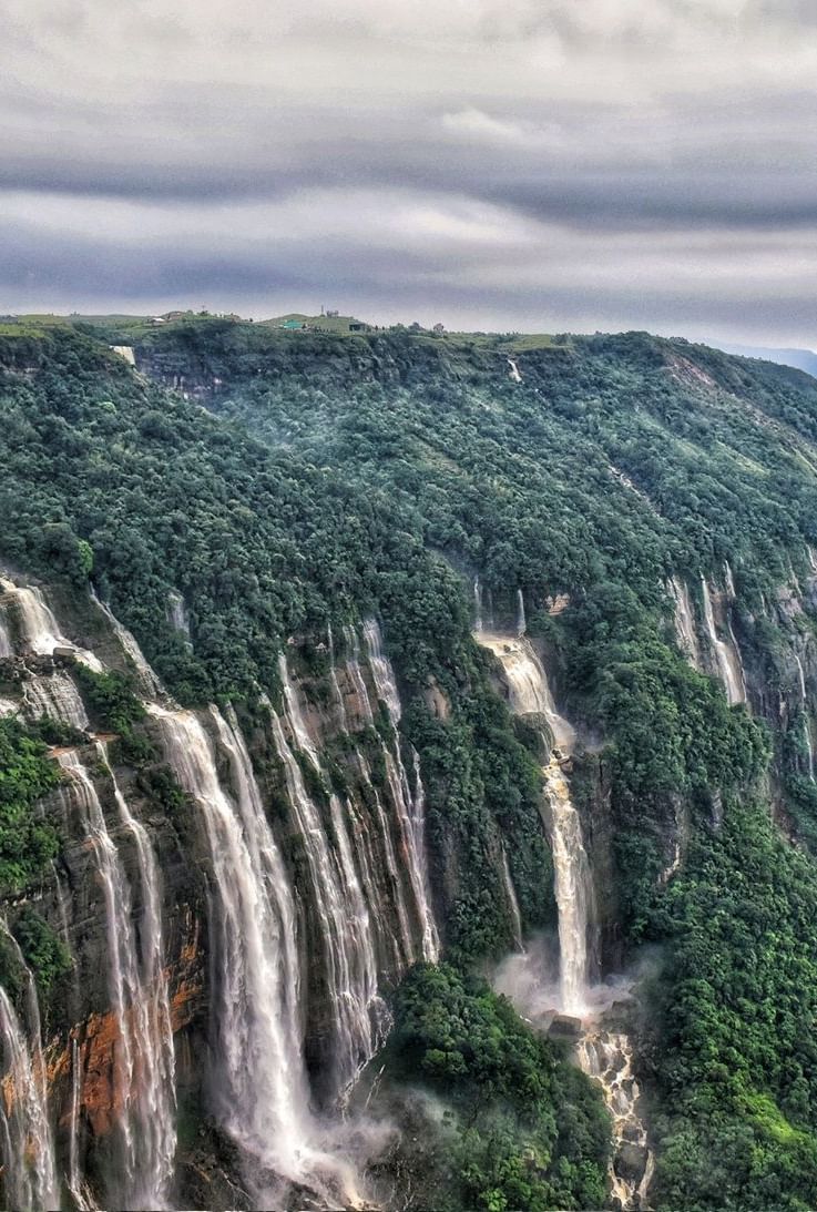 The majestic Seven Sisters waterfalls cascading down steep cliffs covered in dense greenery under a cloudy sky - Polo Hotel Shillong