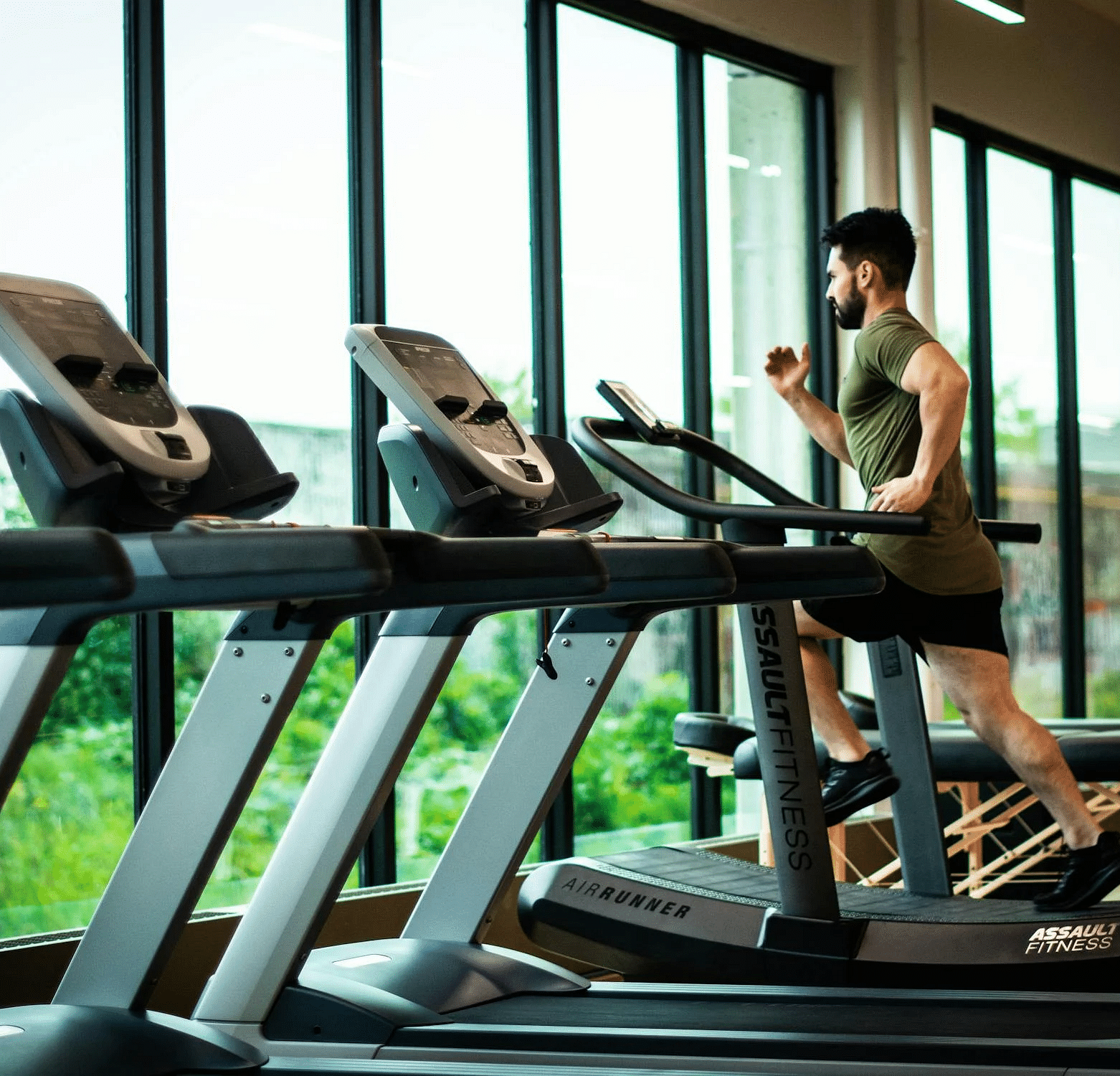 A man running on a treadmill with lush green views outside the huge glass windows.