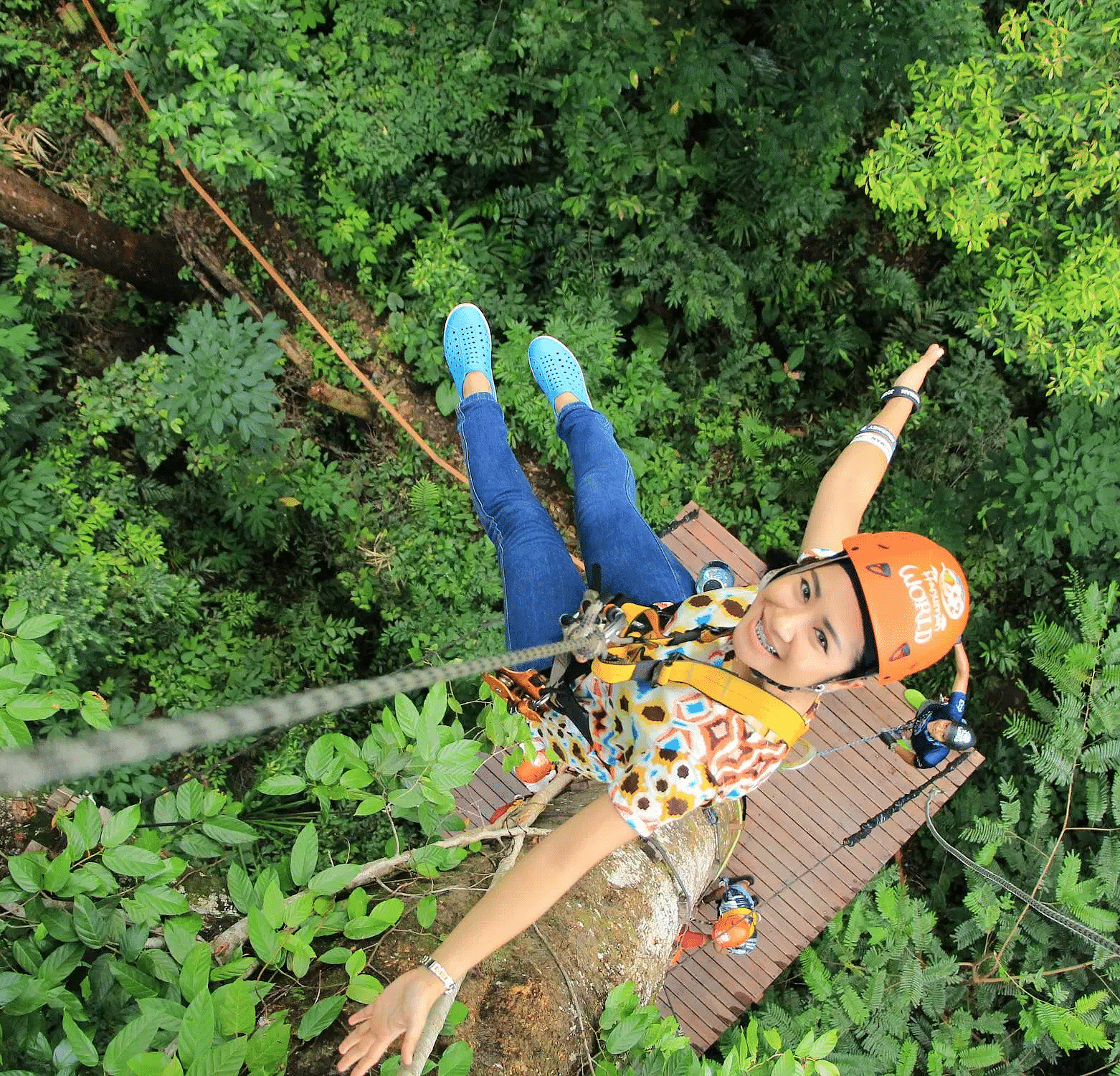 A woman suspended on a rope, soaring above a lush canopy of trees.
