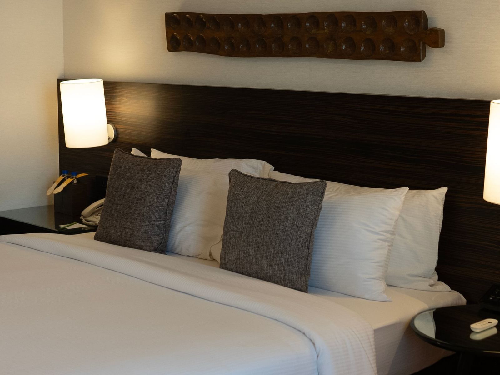 A elegant, bright bedroom at The Raintree, St. Mary's Road, showcasing contemporary design, a bed with white linen and two cushions, bedside lights, and minimalist decor.