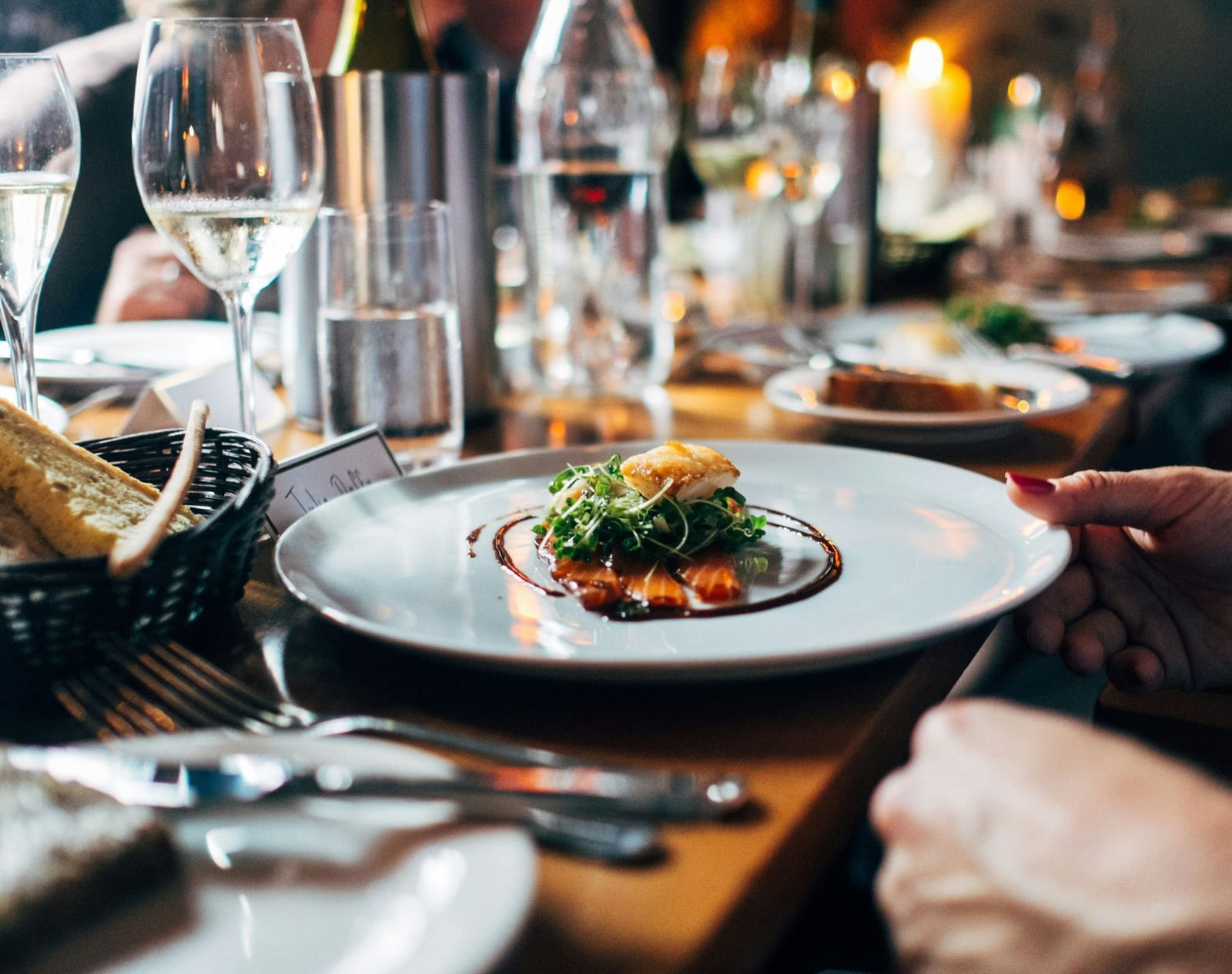 A dish served on a plate in a restaurant with cutlery, wine glasses, bread, and other dining items placed around it.