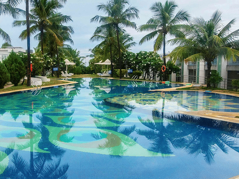 The swimming pool at Grande Bay Resort & Spa, Mamallapuram, surrounded by vibrant greenery with trees beautifully mirrored on the water’s surface.