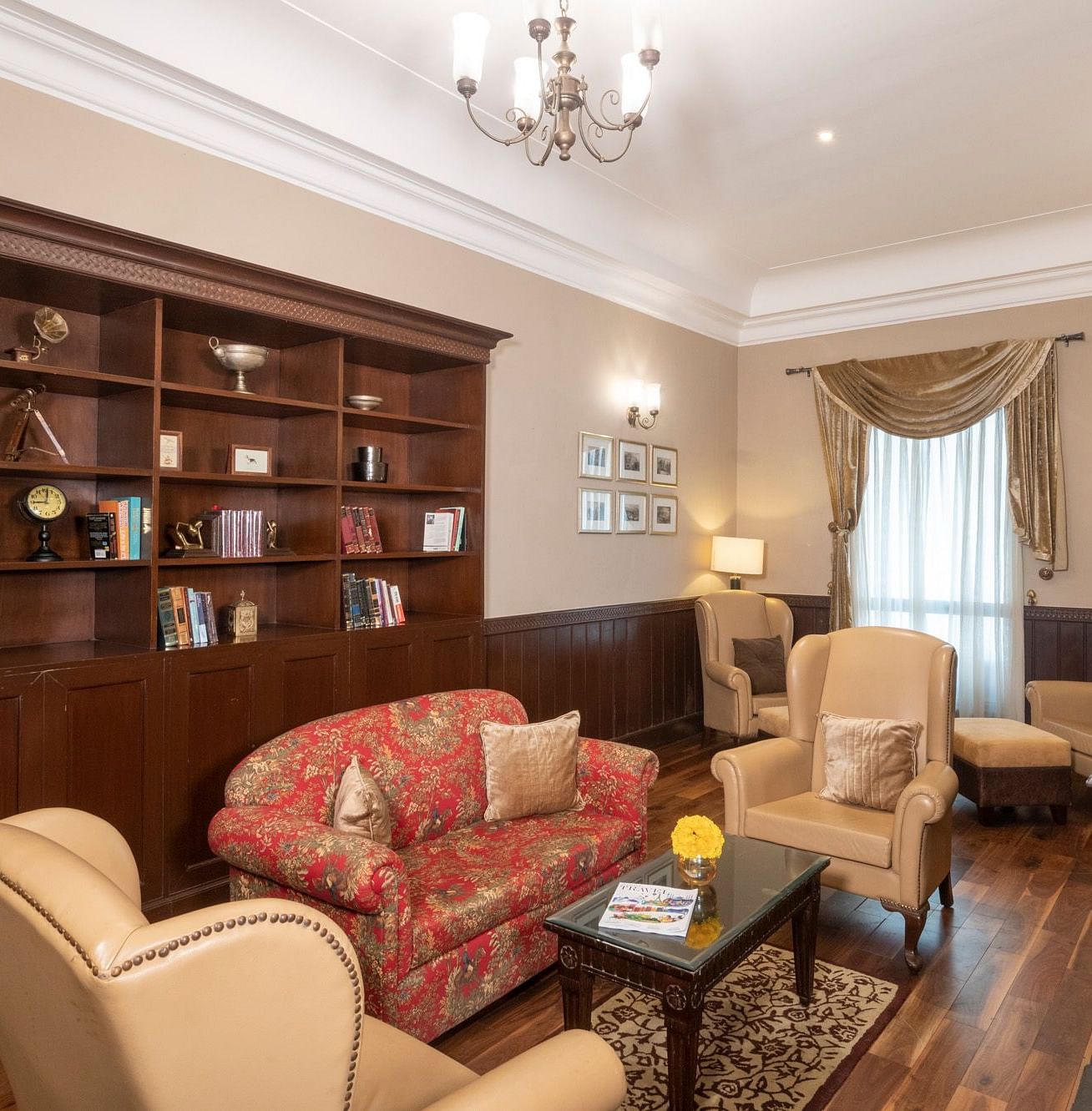 The Library is furnished with classic vintage sofa, two armchairs, a coffee table, a wooden cupboard displaying books, and a window