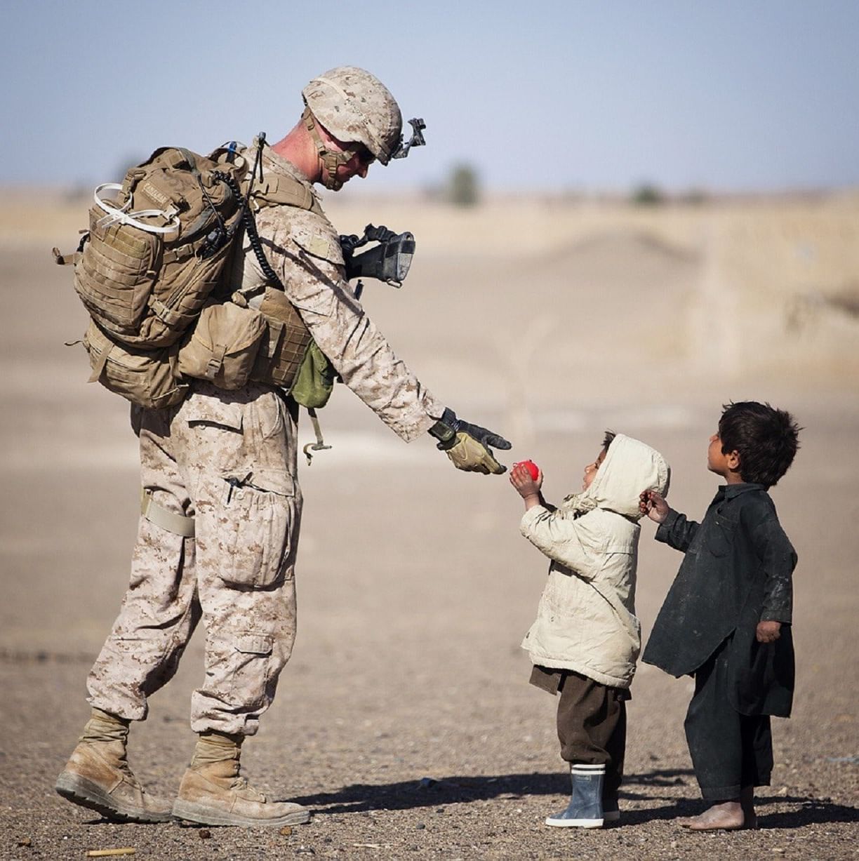 A soldier in an arid region handing over relief supplies to a small toddler