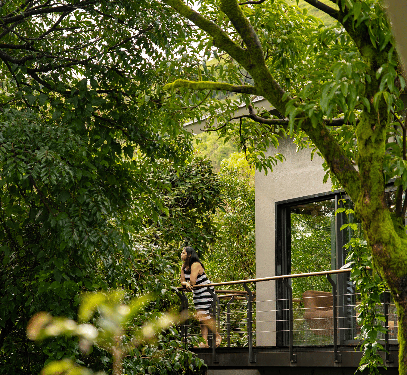 A person stands on a balcony in a modern building at Stanley Revelation, surrounded by lush green trees.