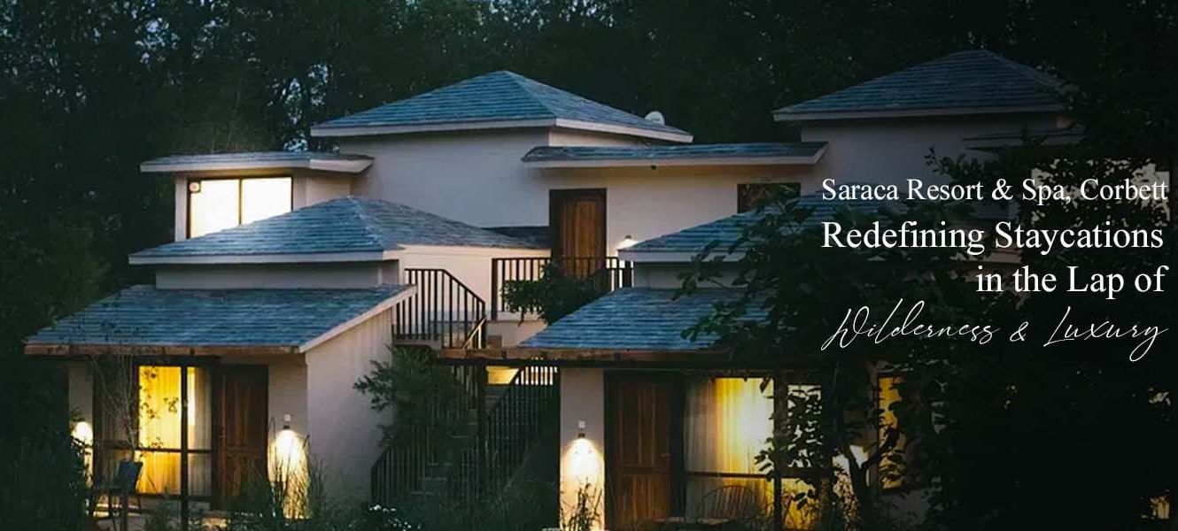 Night view of Saraca Resort & Spa, Corbett, with warmly lit villas surrounded by greenery, text overlay: Saraca Resort & Spa, Corbett: Redefining Staycations in the Lap of Wilderness & Luxury.