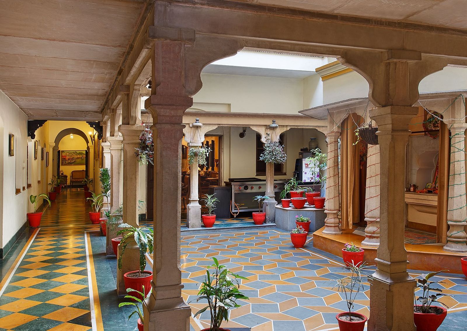 A passage with an open roof space at The Haveli Hari Ganga in Haridwar features block tiles and lush plants, creating a tranquil atmosphere that invites guests to enjoy the beauty of nature while providing shelter and light.