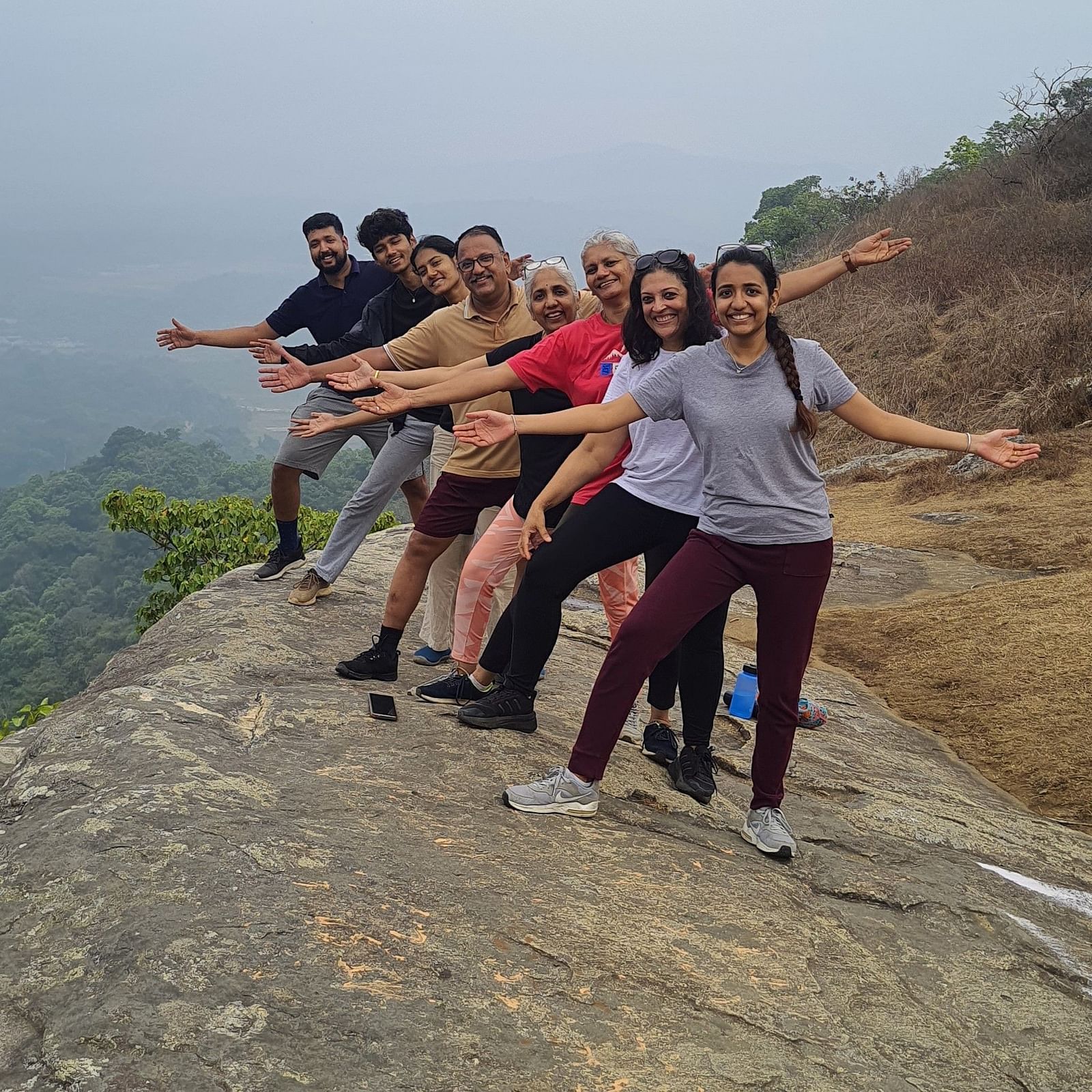 Group of people extending their arms joyfully on a mountain summit with a hazy background - Evergreen County