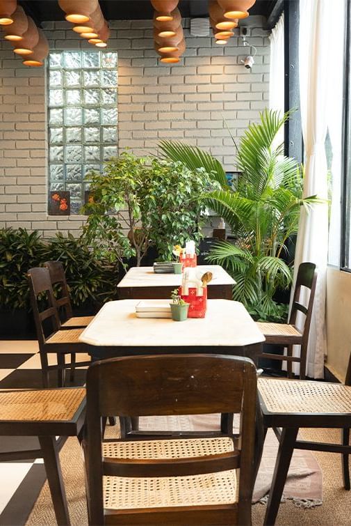 Courtyard-style dining area at Polo Floatel Kolkata with wooden tables, greenery, and natural light.
