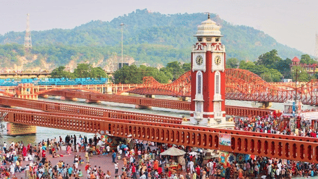 Crowds of pilgrims gathered at Har Ki Pauri in Haridwar with the iconic clock tower and bridges over the River Ganga, capturing the vibrant spiritual atmosphere during the Kumbh Mela near Bhagirathi by Atishay.