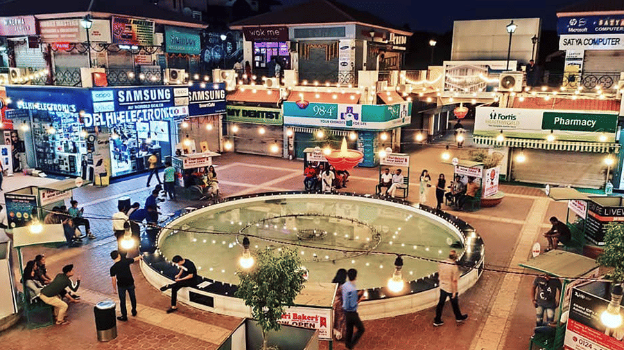 Galleria Market lit up at night, with shopfronts around a circular fountain in Gurgaon