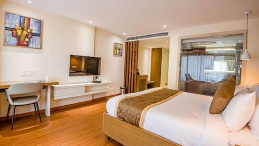 A well-appointed hotel suite with a comfortable bed, a desk area, a large window, and a wall-mounted television, all set within a bright and airy space at Yashshree The Imperial Inn, Siliguri.