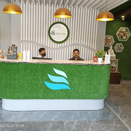 A modern reception area with a desk and three people - Asian Suites IFFCO Chowk Metro Station, Gurgaon. 