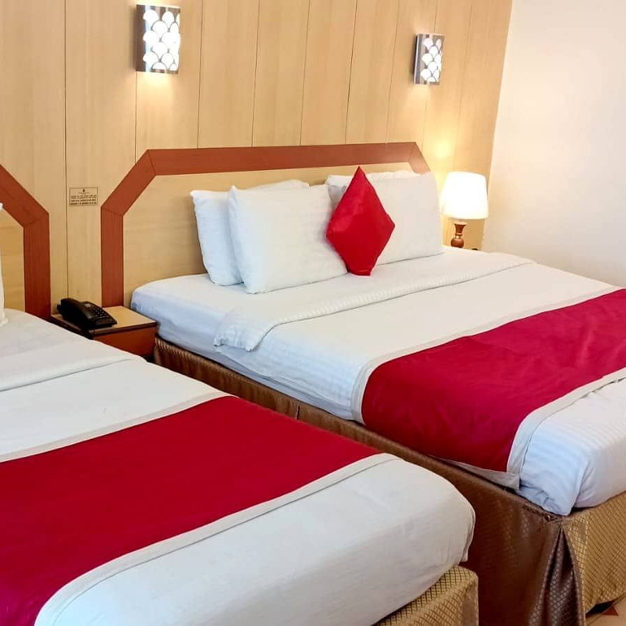 Room with a single bed, a double bed, bedside lamp, and wall-mounted lights at Hotel Swagath, Bangalore