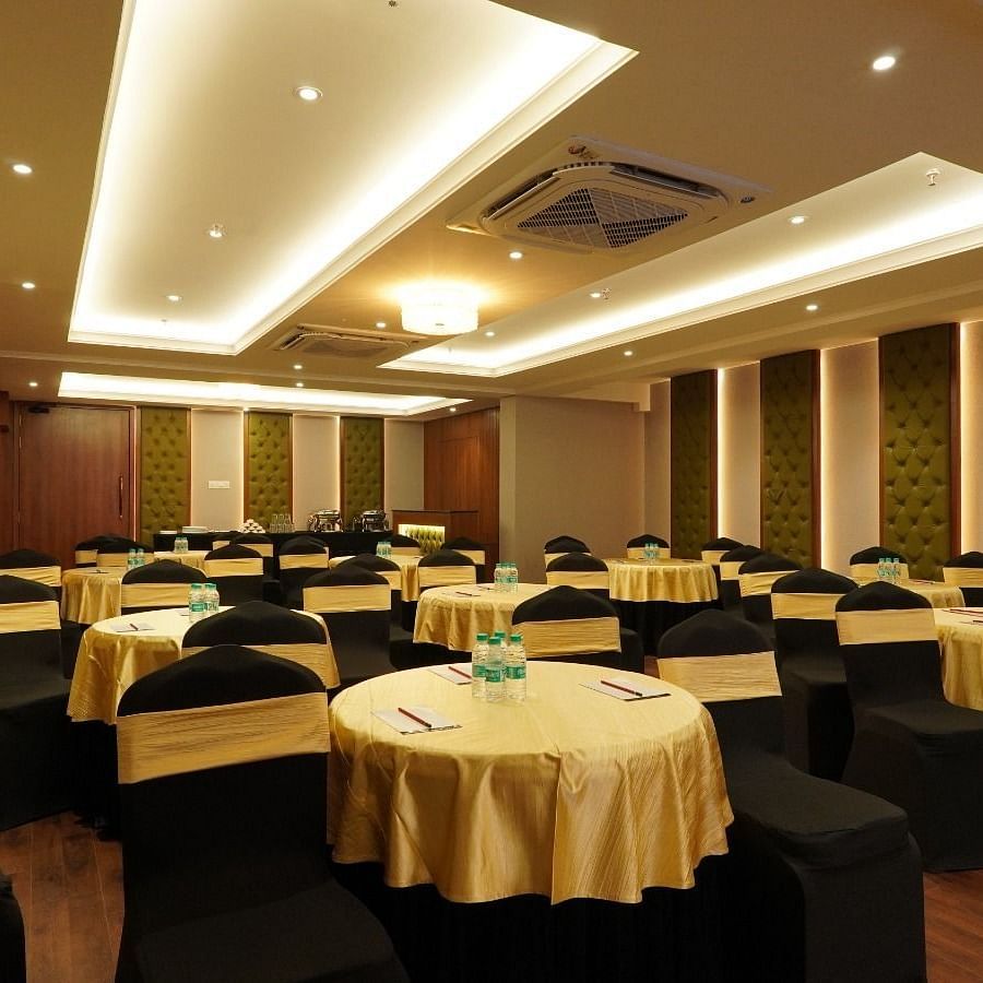 Spacious conference hall with U-shaped wooden table, cushioned black chairs, projector, white screen, and recessed ceiling lights – Magnus Nexstar Suites, Kalyani Nagar