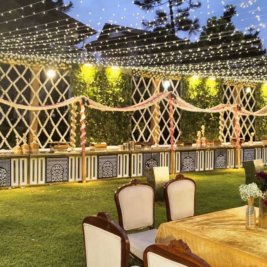 An outdoor dining area with tables, chairs, and a buffet table decorated with lights and greenery.