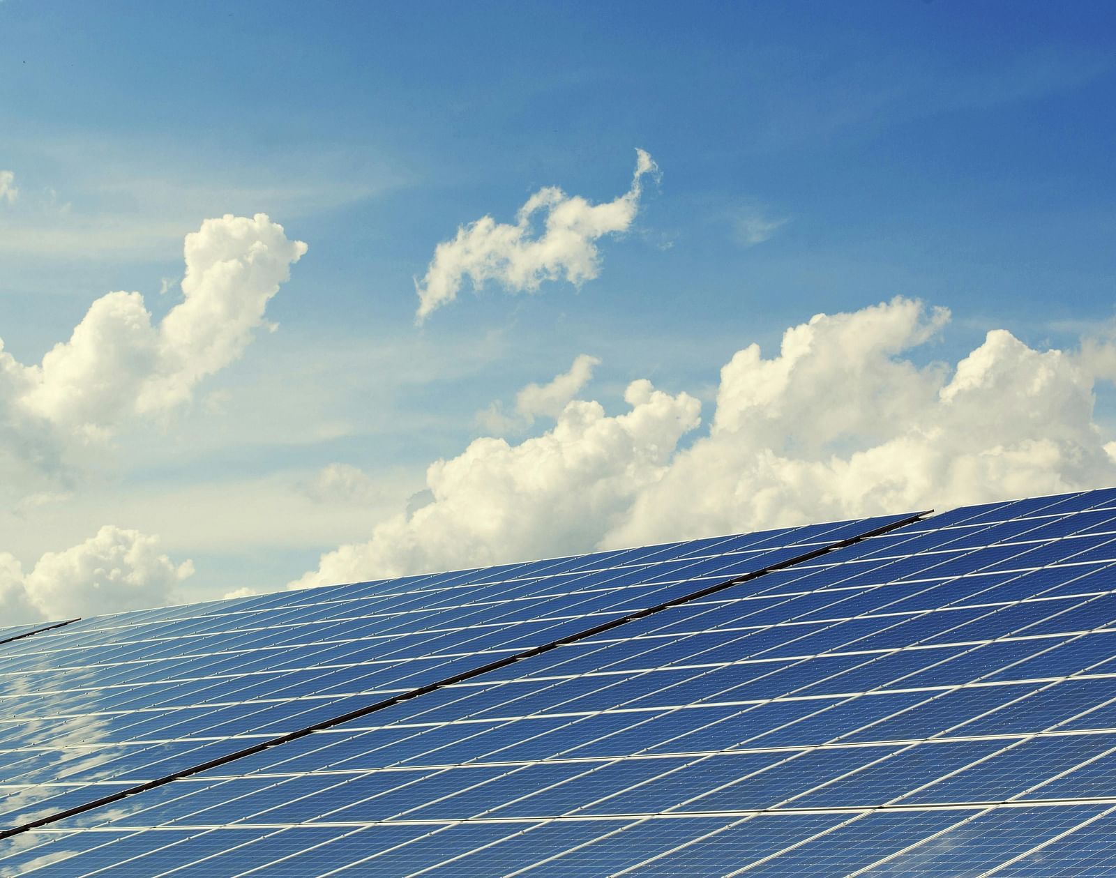 Solar panel array under blue sky with clouds.