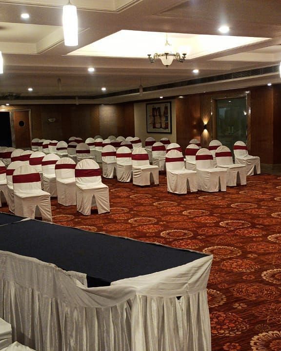 Large banquet hall with rows of chairs arranged, a carpeted floor, and lights on the ceiling, set up for a meeting or event - Lords Plaza Ankleshwar