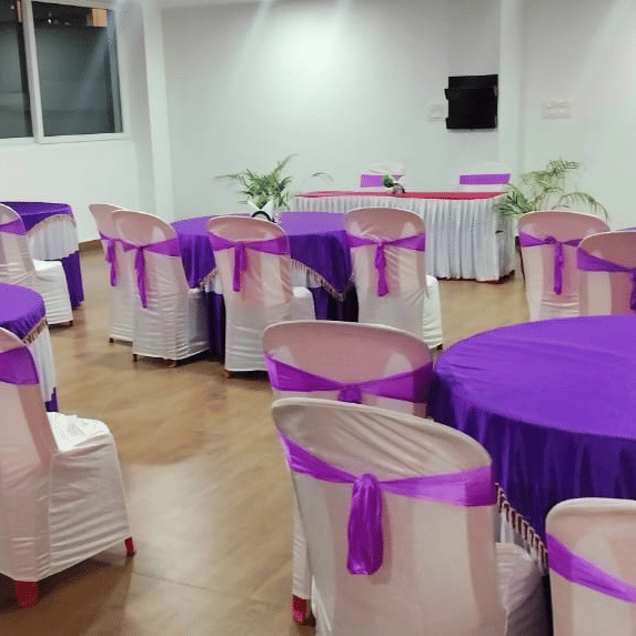 A room set for an event with tables and chairs decorated with striking purple tablecloths and sashes at Coorg Orange Blossom Resort and Spa.