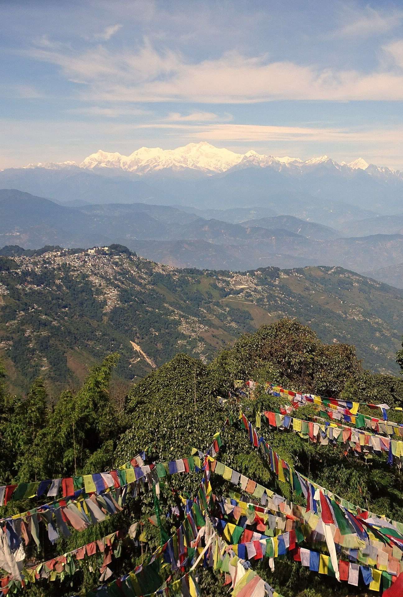 Colourful prayer flags fluttering in the wind, overlooking a panoramic view of valleys and distant mountains.