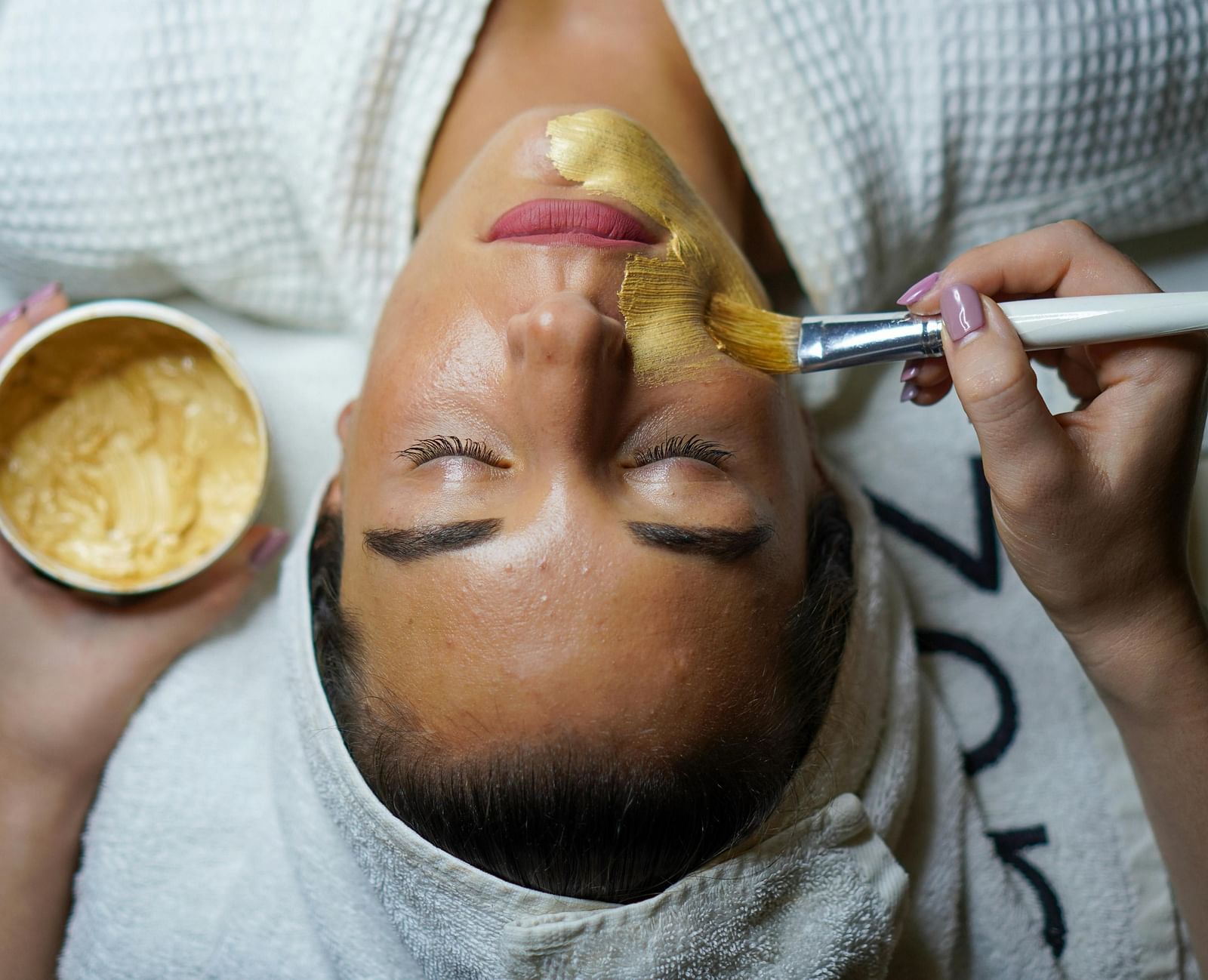 A person receiving a facial treatment with a yellow mask being applied.